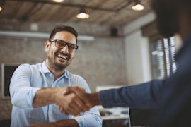 Geschäftsmann schüttelt Hand eines Kunden Geschäftsmann schüttelt Hand eines Kunden zur Begrüßung in einem Microsoft Teams Konferenzraum.